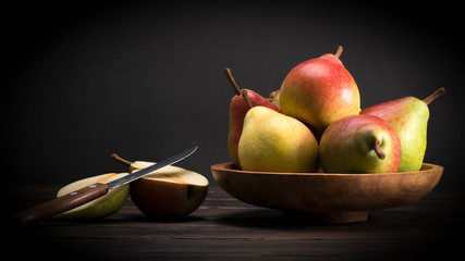 red pears and a yellow pear cut in half with a knife against a black background.