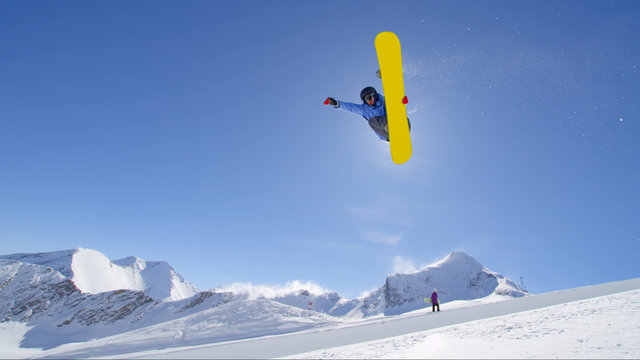 Young pro snowboarder jumping in half pipe in sunny snow park