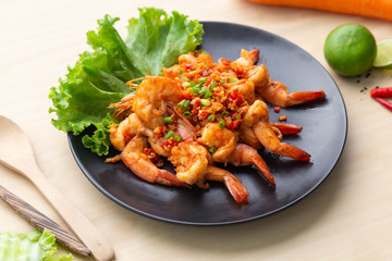 Fried shrimp with pepper and salt in black plate on wooden table, One of famous food in Thailand.