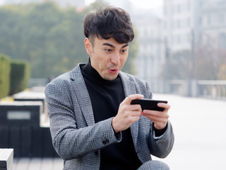 Happy excited young man in suit using cell phone with funny expression, excited business man looking at his smart phone reading good news message email, emotional lifestyle concept.