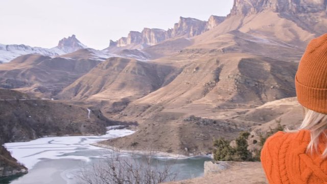 Back view Girl photographer traveler in an orange sweater and hat takes pictures on his dslr camera landscape on the outdor against the backdrop of epic mountains. Travel Photographers Video Concept