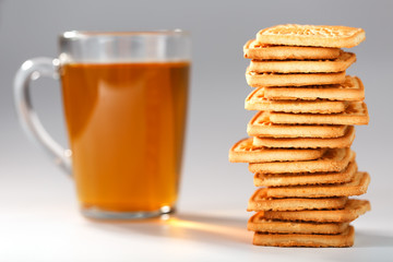 Fototapeta na wymiar A stack of golden wheat cookies and a mug of fragrant green tea in on a gray background. Cookies laid out in a breakfast column and a golden highlight with tea mugs