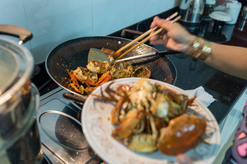 Woman cooking homemade spicy stir-fried crabs in kitchen at home