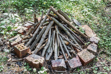 Gray and brown firewood for a bonfire are in a round fire with orange bricks on green grass in a summer forest. like a pyramid