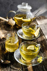 Herbal tea with lemon and honey in glass cup and teapot on sunny day light