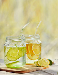Two bottles of cold lemonade with lemon slices and straws with de-focused outdoor background