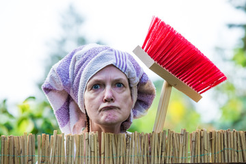 An aggressive, elderly woman with a headscarf and broom scolds at the garden fence. Concept...