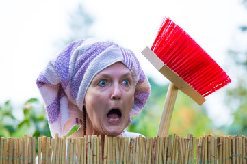 An aggressive, elderly woman with a headscarf and broom scolds at the garden fence. Concept...