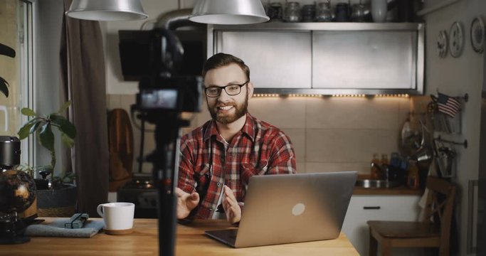 Happy young smiling tech blogger man making vlog video stream with professional camera at home kitchen slow motion.