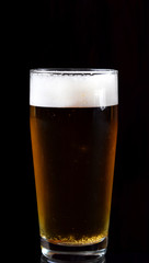 Beer with foam in a tall glass against black background