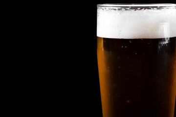 Beer with foam in a tall glass against black background