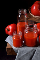 Tomato juice in glass jars on wooden table. Dark photo