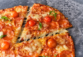 Slice of pepperoni pizza with cherry tomatoes. Sliced tasty pepperoni pizza on the grey stone background. Top view