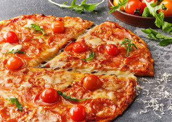 Slice of pepperoni pizza with cherry tomatoes. Sliced tasty pepperoni pizza on the grey stone background.