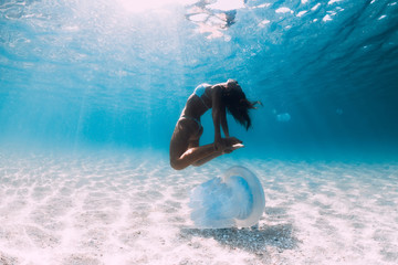 Woman diver glides over sandy sea with jellyfish. Freediving in blue ocean