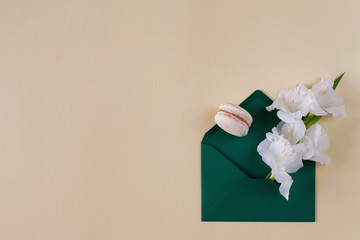 Creative minimalistic flower arrangement. White gladiolus and macaroon in a green envelope on a beige pastel background. Floral design, card or invitation. Copy space, flat lay.