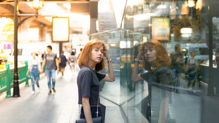 Asian woman Look at window reflect in the city ,bright and orange concept