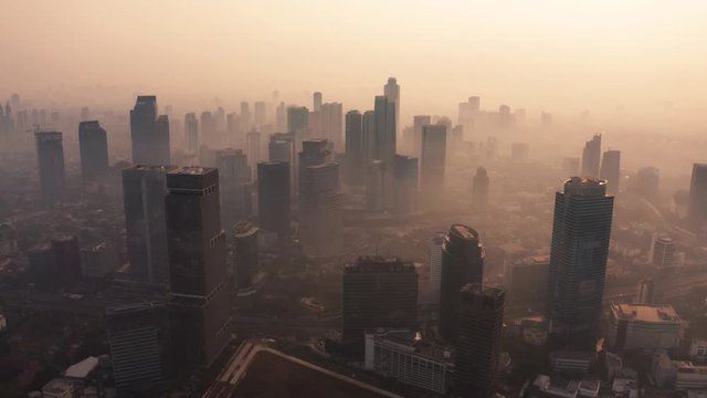 JAKARTA, Indonesia - August 27, 2019: Aerial landscape of dusk time in business district with air pollution fog around office buildings. Shot in 4k resolution from a drone flying forwards