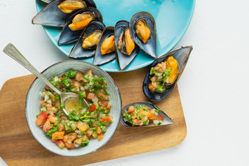 Steamed mussels with onion vinaigrette, tomato and cilantro on white background.