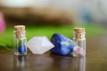 Obraz na płótnie Canvas Miniature crystal vial apothecary set! Mini crystal bottles, Pink and Blue Combo! Azurite Berry, Pink Tourmaline, Rose Quartz, and Sodalite. Healing crystals on plants, wood table in natural lighting