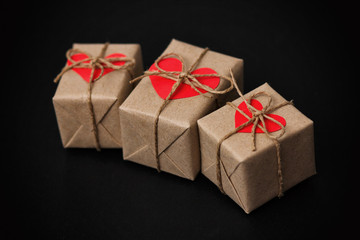 Set of gift boxes on black background. Heart cardboard. Parcels wrapped in craft paper and tie hemp cord.