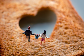 Obraz na płótnie Canvas Love Concept. Miniature of Happy Family Walking on Burned Sliced Toasted Bread with a shape of Heart