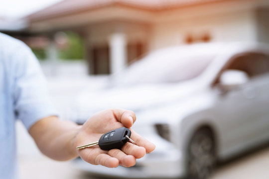 Business man hand holding car keys front with new car on background. parking in front of the house. transportation concept. Leave copy space to write messages text.