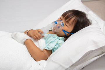 Little Asian girl is sick in a bed with an oxygen mask in hospital