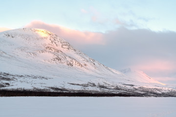 Snow covered mountain Gappetjahkka in Lapland Sweden during sunrise with soft clouds, warm ligth and light sky