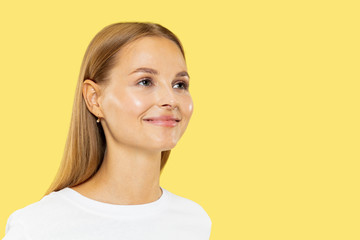 Caucasian young woman's half-length portrait on yellow studio background. Beautiful female model in white shirt. Concept of human emotions, facial expression, sales. Smiling, looking at side.