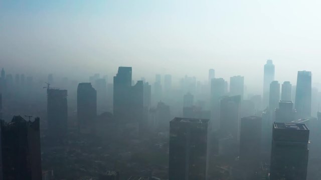 JAKARTA, Indonesia - August 27, 2019: Aerial view of unhealthy city with dense air pollution smoke and silhouette of skyscrapers. Shot in 4k resolution from a drone flying forwards