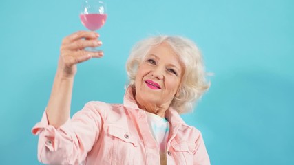 Happy positive grandma with glass looking at the camera, celebrating her birthday. Happiness, positive emotion and feeling. Isolated blue background