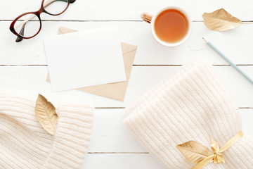 Cozy home desk table with knitted plaid, tea cup, fall leaves, letter with blank card on wooden...
