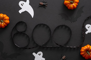 Halloween decorations, pumpkins, ghosts, text sign "BOO" on black background. Halloween concept. Flat lay, top view, overhead.