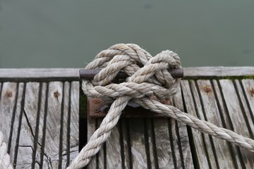 Fototapeta premium A rusty bollard with a rope tied to it by a sea knot on the edge of a wooden pier. Summer day on Beloe lake.