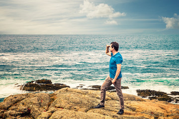 man standing on the rocks next to the rough sea looking at the horizon