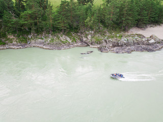 Aerial view of a rubber motor boat sailing on a green river in the mountains between rocks and cliff