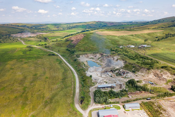 Aerial view of a small plant for the production and cleaning rubble and cement near the heaps of building materials from the pipe of which gray smoke goes, the tractor transports the finished product.
