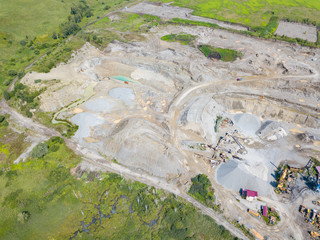 Aerial view of a small plant for the production and cleaning rubble and cement near the heaps of building materials from the pipe of which gray smoke goes, the tractor transports the finished product.