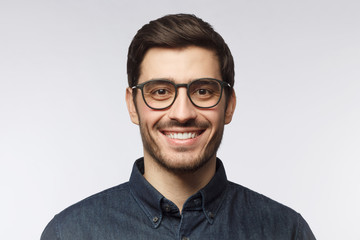 Headshot of smiling handsome man with trendy haircut and glasses isolated on gray background