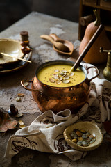 pumpkin yellow soup puree with pumpkin seeds on top in copper pan