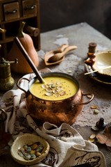 pumpkin yellow soup puree with pumpkin seeds on top in copper pan