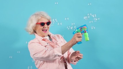 Funny stylish glamour granny in sunglasses making soap bubbles. Lifestyle, spare time.