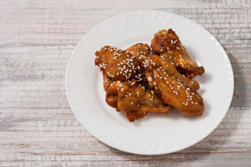 Fried juicy chicken wings marinated with honey, soy sauce, spices, sprinkled with sesame seeds on a white plate on a light background. Asian recipe, top view, close up