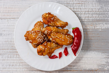 Fried juicy chicken wings marinated with honey, soy sauce, spices, sprinkled with sesame seeds on a white plate on a light background. Asian recipe, top view, close up