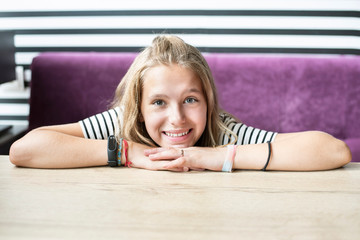 Portrait of a beautiful young girl with blond hair sitting in a cafe waiting for her dessert. Girl sincerely smiles