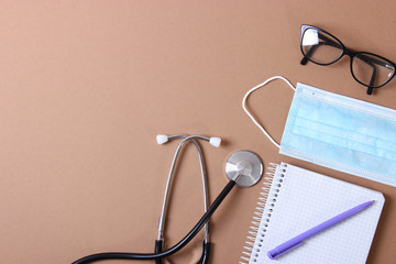 Doctor's desk top view. Stethoscope, pills, glasses and notebook on a colored background.