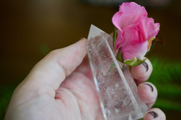 Beautiful Clear Quartz tower, and fresh pink rose flowers. Bright Quartz crystal, healing crystal being held in hand. Woman holding quartz tower, crisp colors in natural lighting. Vibrant meditation.