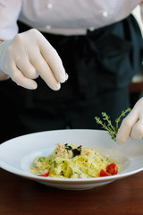 Chief dressing pasta with black truffle and herbs.