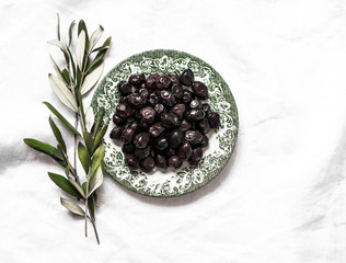 Dried black olives on a vintage plate on a light background, top view